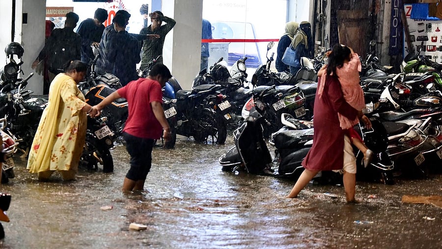 Commuters wade through a waterlogged street following rain in Hyderabad. Credit: PTI Photo