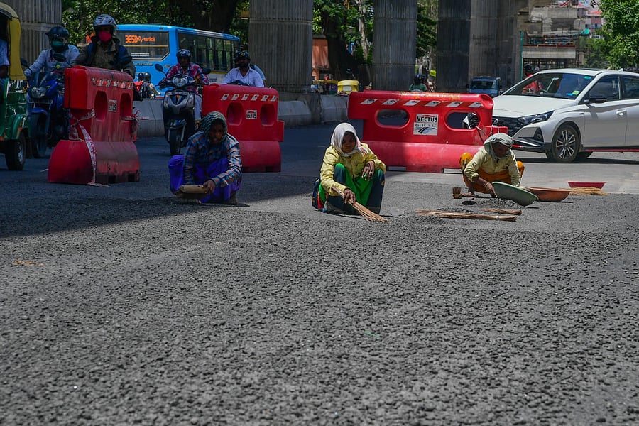 Women workers cleaning waste partials came out after asphalt laying at Toll gate, Bannerghatta Road in Bengaluru. Credit: DH File Photo