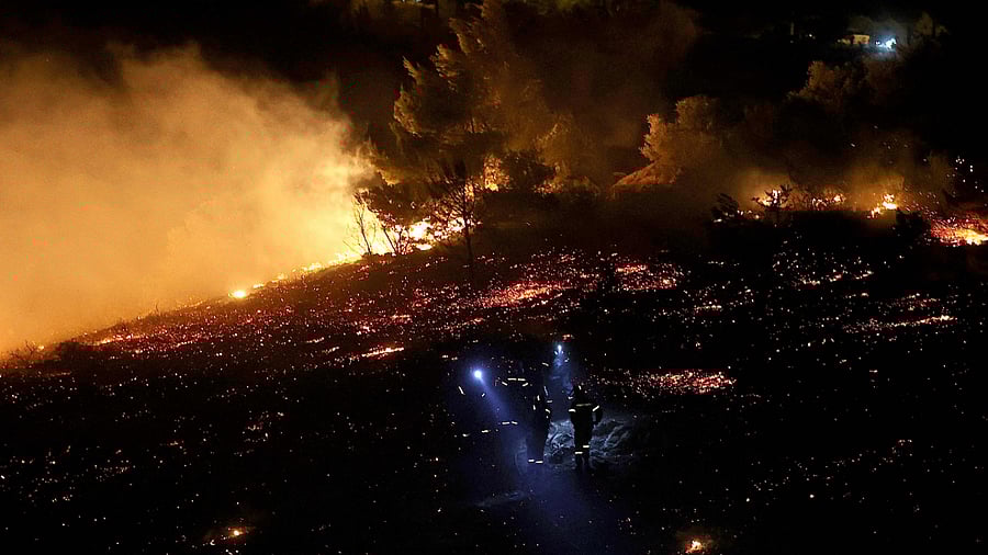 Firefighters use headlamps as they stand in ash as a wildfire rages in Anthousa, north of Athens, on July 19, 2022. Credit: AFP Photo