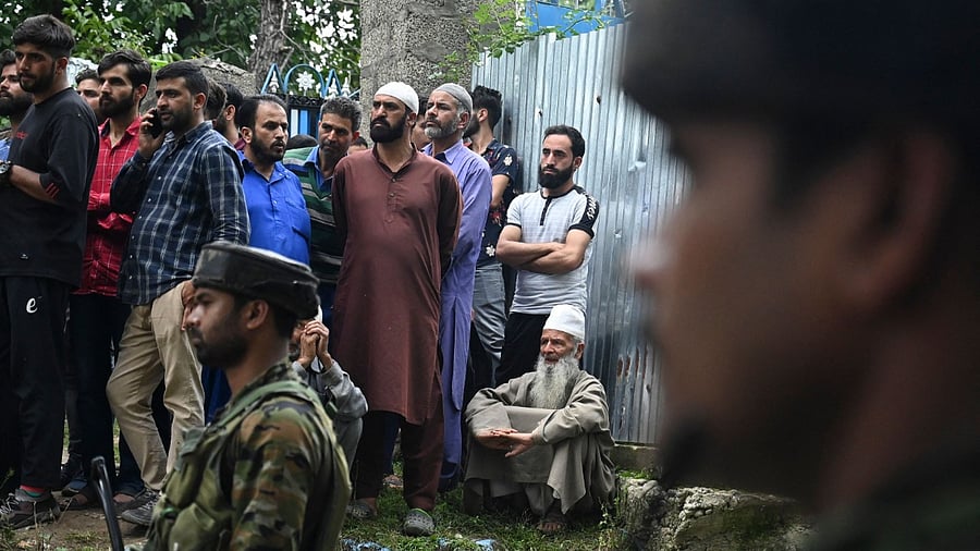 Security forces stand guard as neighbours gather outside the house of Sunil Kumar, who belonged to the Kashmiri Pandit community, after militants shot him dead at an apple orchard in Chotipora area of Shopian. Credit: AFP Photo