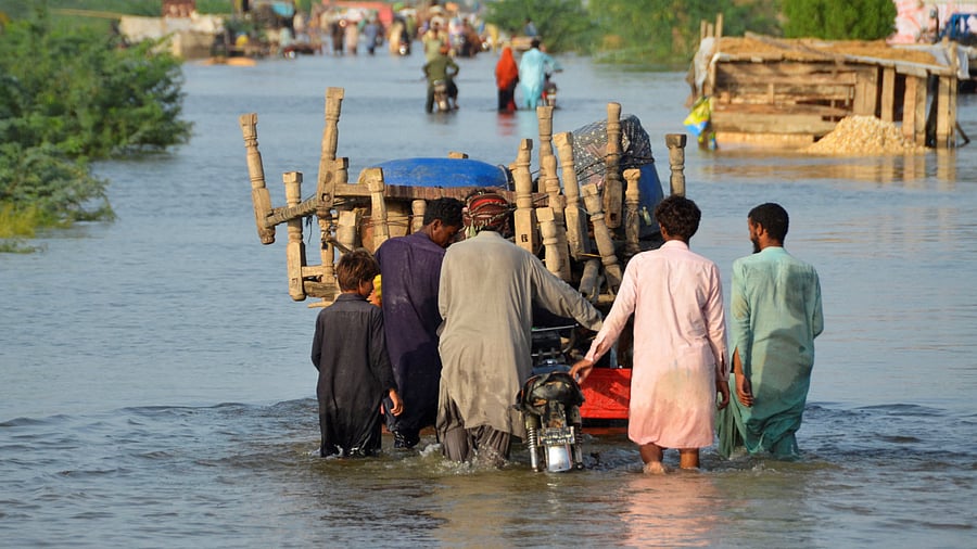 Men walk along a flooded road with their belongings, following rains and floods during the monsoon season in Suhbatpur. Credit: Reuters Photo