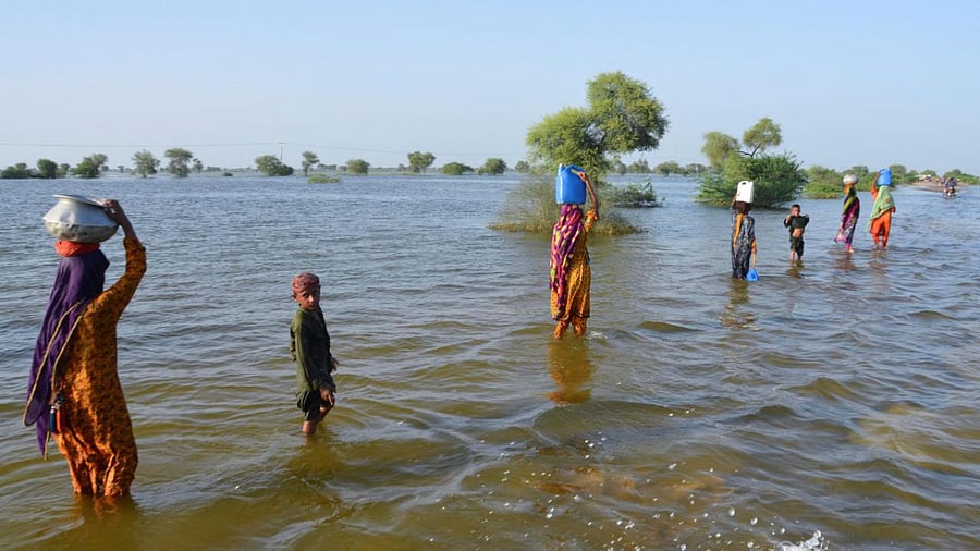Flood victims carry water in pots and jerrycans as they walk on a flooded road, following rains and floods during the monsoon season in Sohbatpur, Pakistan. Credit: Reuters Photo