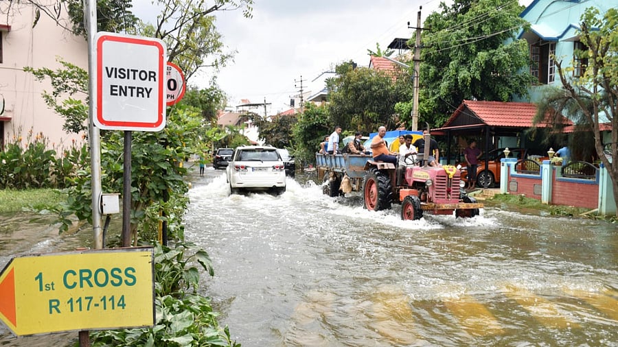 Residents of the Rainbow drive using transport by a tractor after flooded during Halanayakanahalli lake breached on Sarjapura main road in Bengaluru on Thursday. Credit: DH Photo