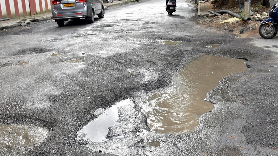 Commuters drive vehicles through potholes on Gangadhar Chetty road after recent heavy rains at Halasuru in Bengaluru. (For representative purpose) Credit: DH Photo/BK Janardhan