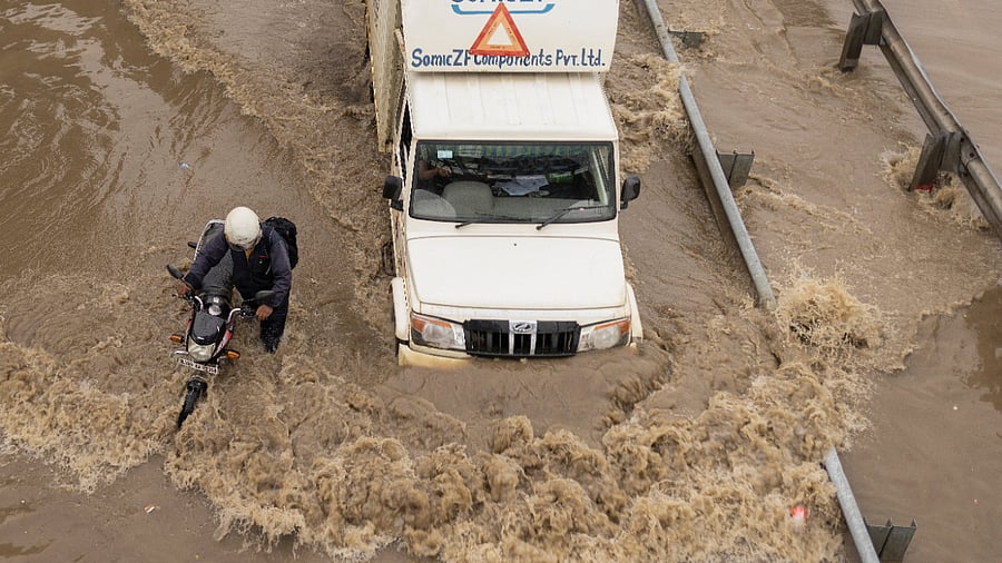 A man pushes his stalled motorbike on a flooded street as a truck drives past after heavy rains in Gurugram, on the outskirts of New Delhi, September 23, 2022. Credit: Reuters Photo