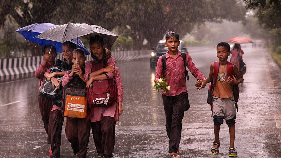 Students holding umbrellas walk down a road amid rainfall, in Noida on September 22. Credit: PTI Photo