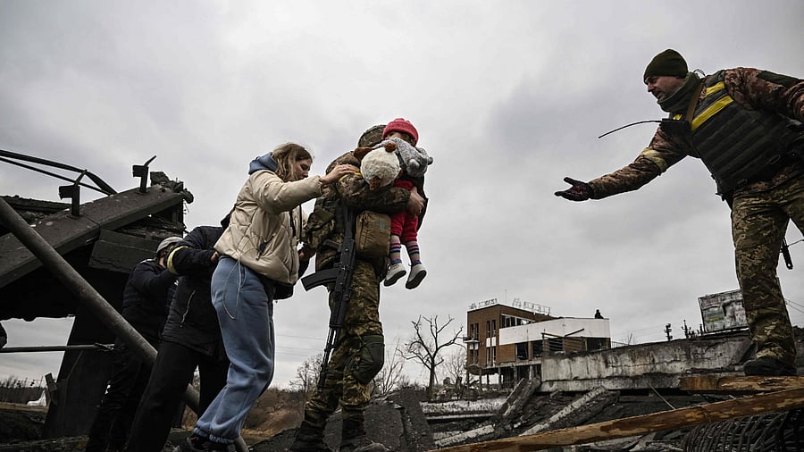A Ukrainian serviceman carries a child while assisting people to cross a destroyed bridge as they evacuate the city of Irpin, northwest of Kyiv. Credit: AP Photo