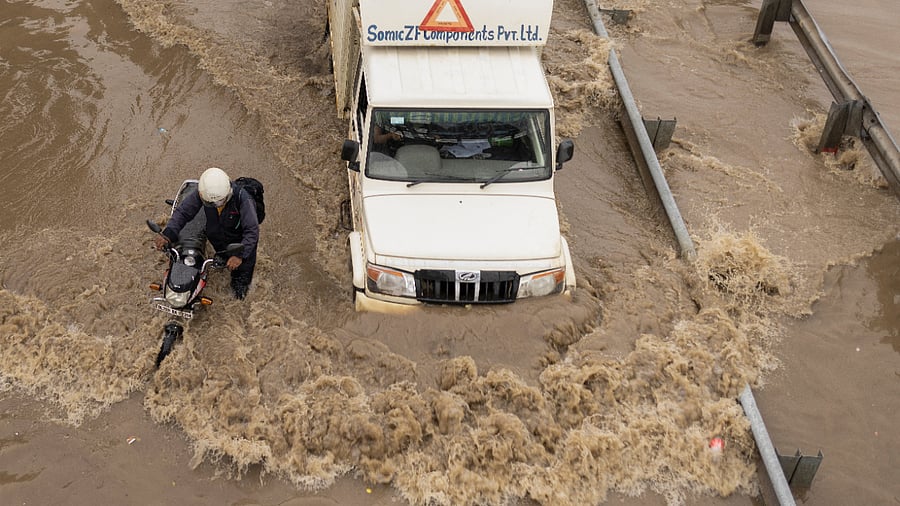 A man pushes his stalled motorbike on a flooded street as a truck drives past after heavy on outskirts of New Delhi. Credit: Reuters Photo