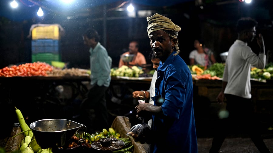 A vegetable vendor gestures at a market as it rains in New Delhi on October 9, 2022. Credit: AFP Photo