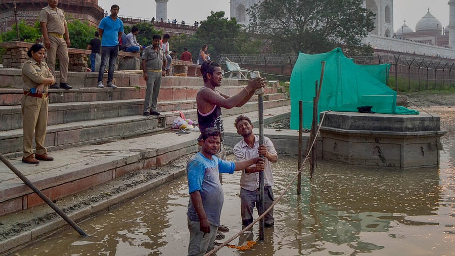 Police person stand guard as workers prepare a bank of Yamuna river for Durga idol immersion, in the backdrop of Taj Mahal, in Agra. Credit: PTI Photo