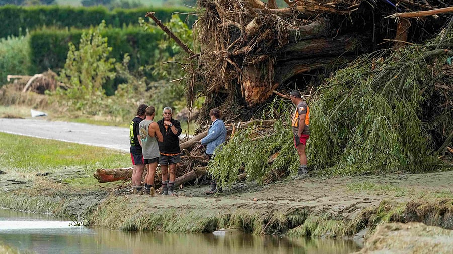 This photo shows people standing next to debris in a flood-affected area in the aftermath of Cyclone Gabrielle near Napier. Credit: AFP Photo