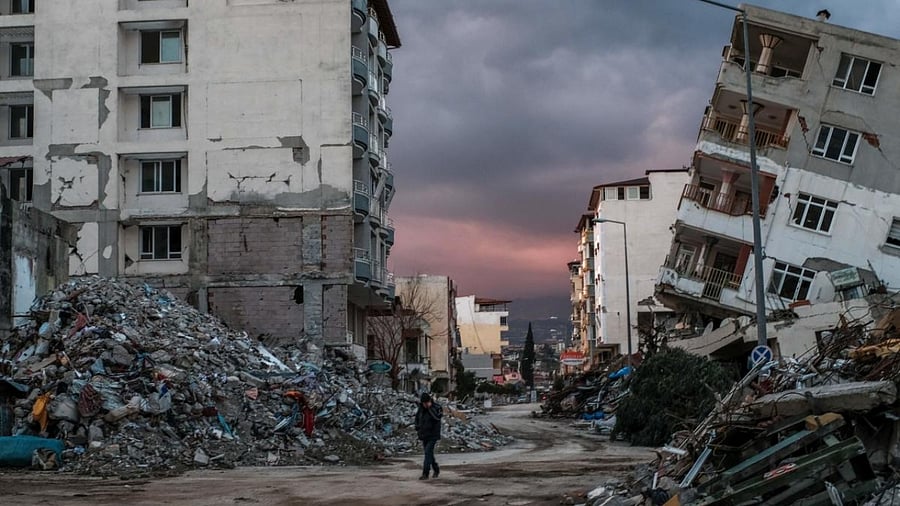 A man walks among collapsed buildings, a day after a 6.4-magnitude earthquake struck the region, in the coastal city of Samandag on February 21, 2023. Credit: AFP Photo