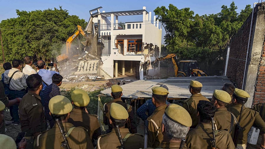 Police personnel watch as a Prayagraj Development Authority bulldozer demolishes Maskuddin's properties in the Sallahpur village near Bamrauli, in Prayagraj. Credit: PTI Photo