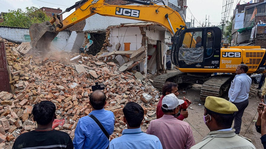Police and media watch as a Prayagraj Development Authority bulldozer demolishes properties of Mohammad Gulam, a close aide of Atique Ahmad and accused in Umesh Pal murder case, in Prayagraj, Monday, March 20, 2023. Credit: PTI Photo