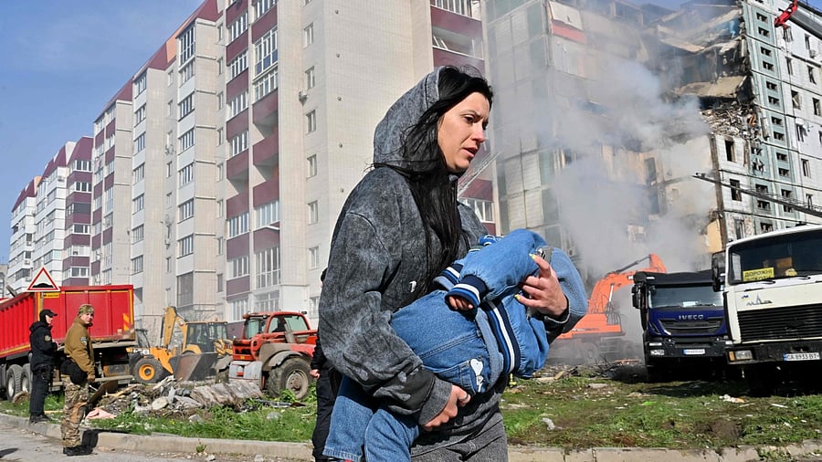 A woman walks past damaged residential buildings as she carries a child in Uman, around 215km southern Kyiv, on April 28, 2023. Credit: AFP Photo