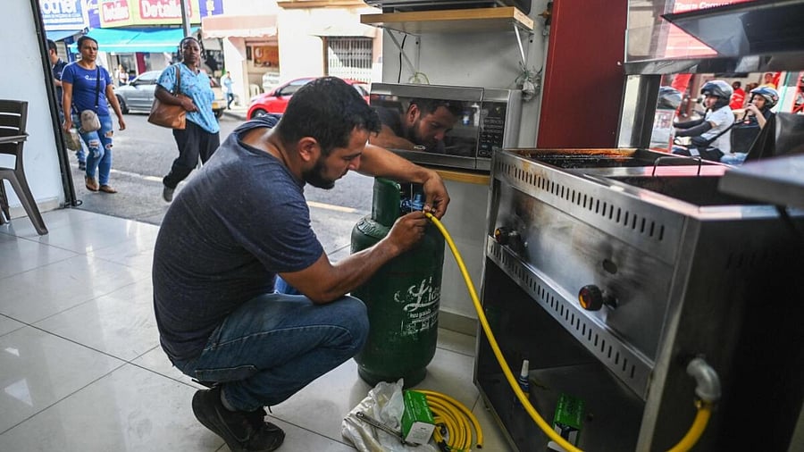 A man connects a gas cylinder to a frier in Cali, Colombia on May 24, 2023. Credit: AFP Photo