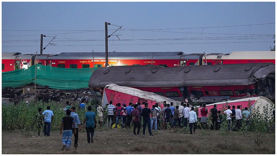  Locals watch a train running past the mangled coaches at the triple train mishap site. Credit: PTI Photo