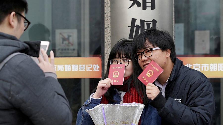 A new couple holding marriage certificates poses for a photo outside a registry office of marriage on Valentine's Day in Beijing, China, February 14, 2017. Credit: Reuters File Photo