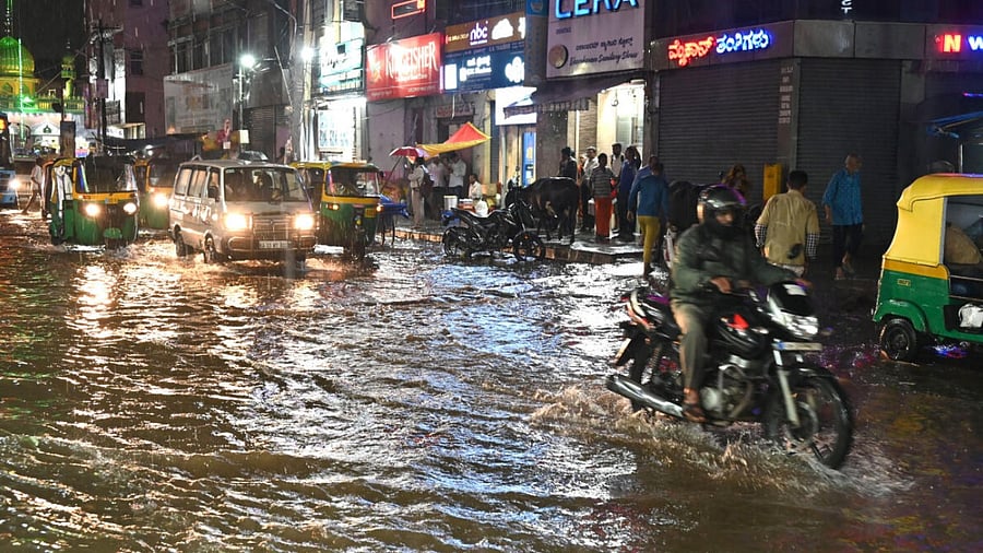 People struggle to reach their destination in heavy rain and rain water flooded on the road at SJP Road in Bengaluru. credit: DH Photo