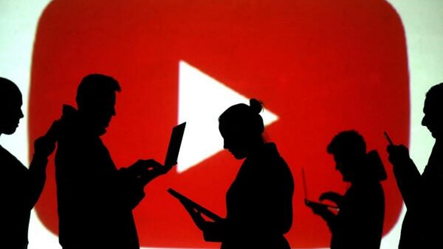 Silhouettes of laptop and mobile device users next to a screen projection of the YouTube logo in this picture illustration. Credit: Reuters File Photo