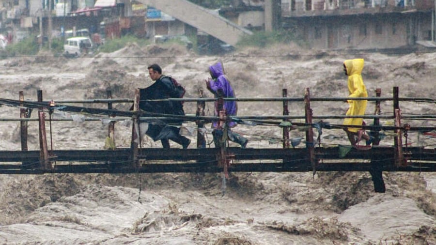 Locals cross a bridge over the swollen Beas river during heavy rainfall, in Kullu district, Monday, July 10, 2023. Credit: PTI Photo
