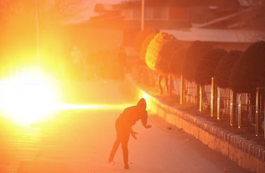 A demonstrator throws a stone towards Indian police (unseen) as a teargas shell fired by police explodes behind him during a protest after India's National Investigation Agency (NIA) summons Mirwaiz Umar Farooq, chairman of Kashmir's moderate faction of All Parties Hurriyat (Freedom) Conference (APHC), in Srinagar, March 10, 2019. REUTERS/Danish Ismail 