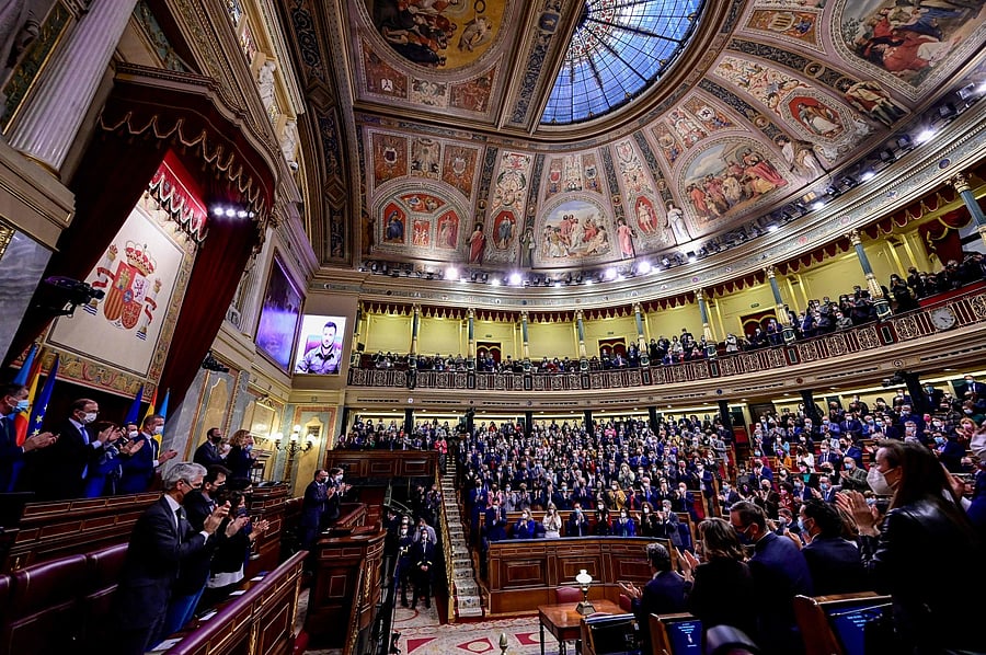Ukrainian President Volodymyr Zelensky (Top-L) receives a standing ovation as he appears on a screen to address the lower house by videoconference, at the Spanish Parliament in Madrid. Credit: AFP Photo
