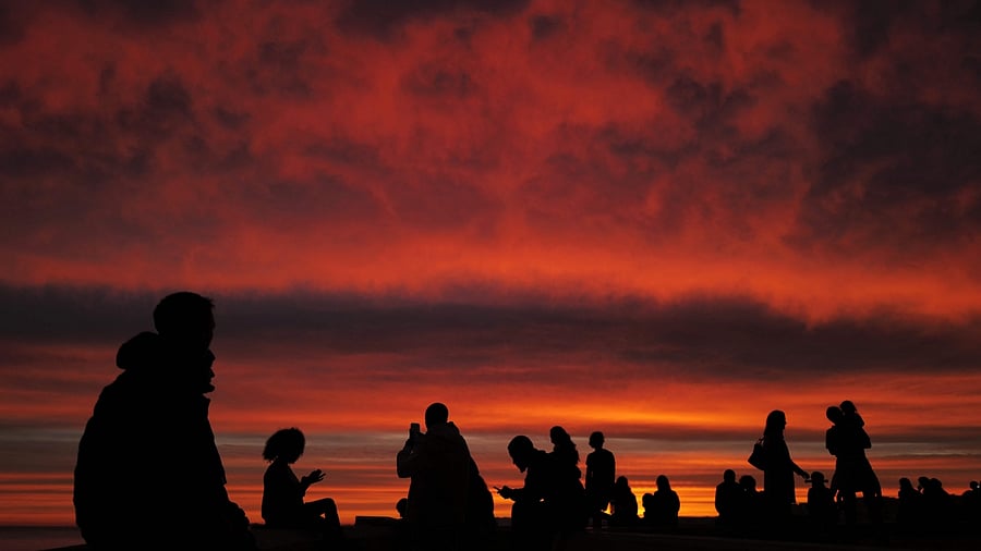Pedestrians walk look at the Mediterranean sea with a sunset in the background on the 'Promenade des anglais' of the French riviera city of Nice, on November 12, 2022. Credit: AFP Photo