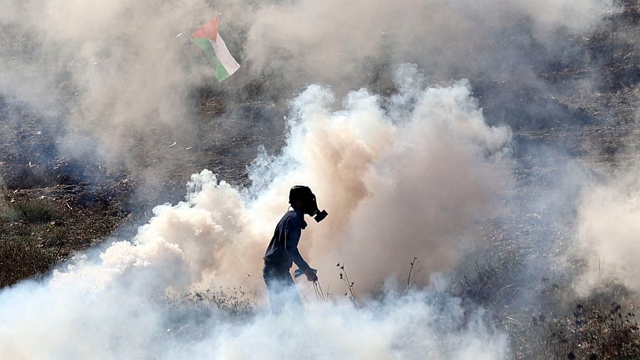 A Palestinian demonstrator wearing a gas mask stands amidst tear gas smoke fired by Israeli soldiers during clashes following a protest against the establishment of Israeli outposts, in Beit Dajan, east of the occupied West Bank city of Nablus, on December 16, 2022. Credit: AFP Photo