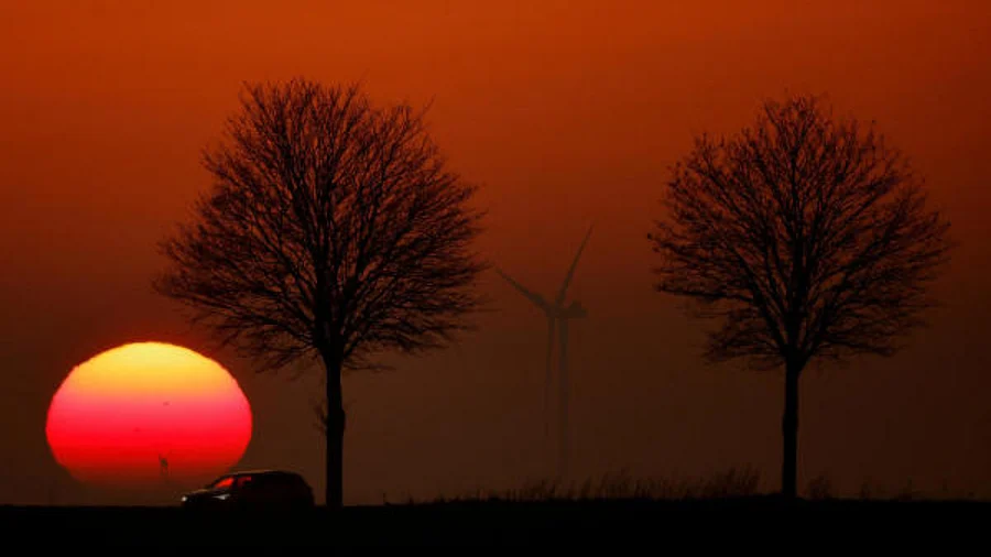 A car drives in front of power-generating windmill turbines on the Cambrai-Arras road during sunset in Epinoy. Credit: Reuters Photo