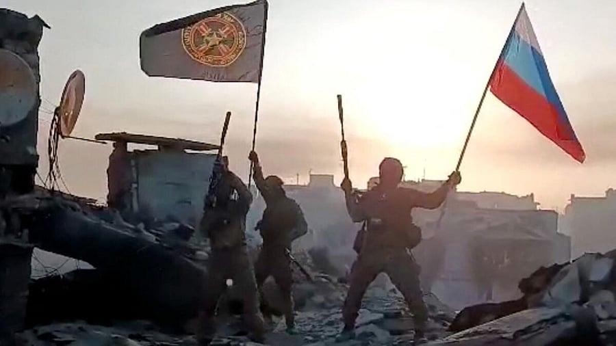 This video grab taken from a handout footage posted on May 20, 2023 on the Telegram account of the press service of Concord -- a company linked to the chief of Russian mercenary group Wagner, Yevgeny Prigozhin -- shows members of Wagner group waving a Russian national flag and Wagner Group's flag on the rooftop of a damaged building in Bakhmut, amid the Russian invasion of Ukraine. Credit: AFP Photo