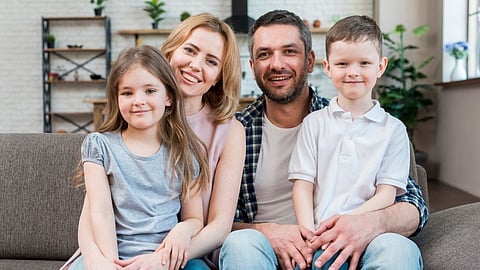 Two adults and two children sitting together on a sofa at home.