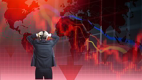 Businessman in suit holding head in front of red world map and falling stock market graphs, symbolizing global financial crisis and stock market crash