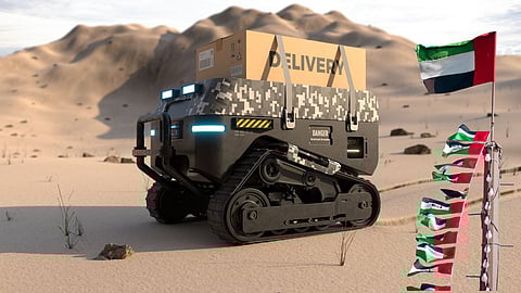 Autonomous delivery robot with camouflage design carrying a package marked “DELIVERY” across a desert landscape, with UAE flag and other regional flags in the foreground.