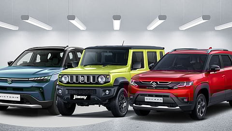 Line-up of Maruti Suzuki cars displayed in a showroom setting, including the blue Maruti Suzuki Victoris, green Maruti Suzuki Jimny, and red Maruti Suzuki Brezza