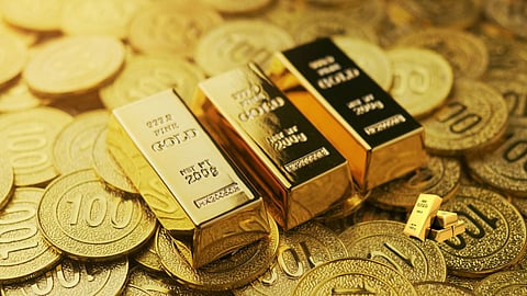 Close-up view of shiny gold bars placed on a pile of gold coins, symbolising wealth, investment, and rising gold prices.
