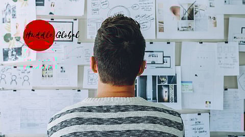 Man brainstorming startup ideas in front of a wall filled with business plans and design sketches, featuring the Huddle Global logo symbolising innovation and entrepreneurship