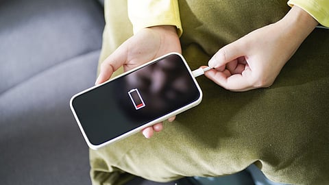 Person charging a smartphone with a low-battery warning icon displayed on screen