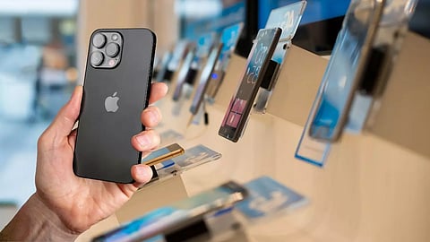 A person holding a black Apple iPhone in a smartphone retail store, with multiple display phones lined up in the background