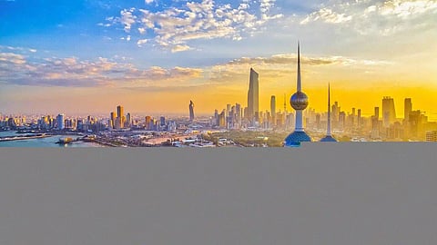 Skyline of Kuwait City with modern skyscrapers and illuminated buildings against a sunset sky.