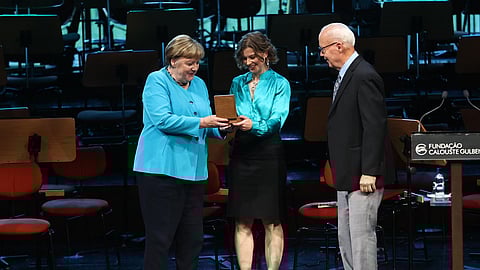 A antiga chanceler alemã, Angela Merkel, entrega o prémio à diretora-executiva da ASOC, Claire Christian, e ao cofundador, Jim Barnes.