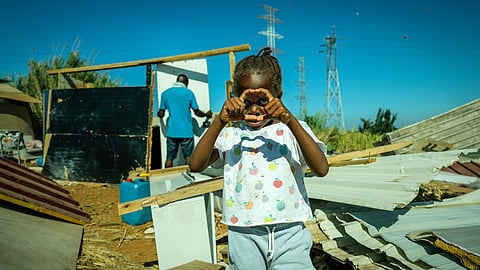 Uma das crianças, filha de moradores do Talude Militar, brinca livremente, enquanto Manuel, um dos moradores que vive sozinho, reconstrói a sua habitação antes do anoitecer.