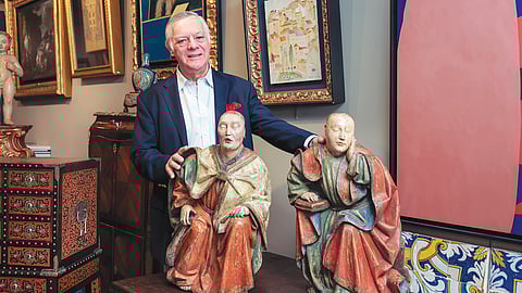 Galerista Mário Roque com duas figuras de traços chineses em madeira a representar São Lucas e São João Evangelista.