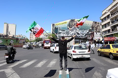 Um iraniano agita bandeiras do seu país com imagens de ayatollahs, em Teerão.