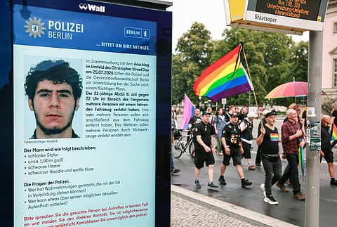 Marcha de luto em Berlim passa ao lado de cartaz da polícia com identificação do suspeito do atentado da véspera.