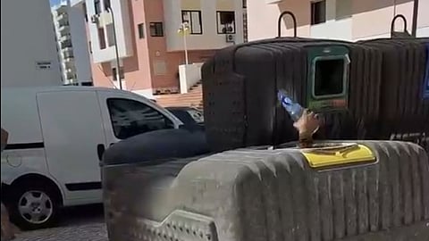 Um 'mineiro do lixo', na Quarteira, derrubou um contentor de plásticos, no qual entrou e, partir do interior, seleciona e atira para fora as embalagens que vai recolher depois e devolver aos pontos de entrega.