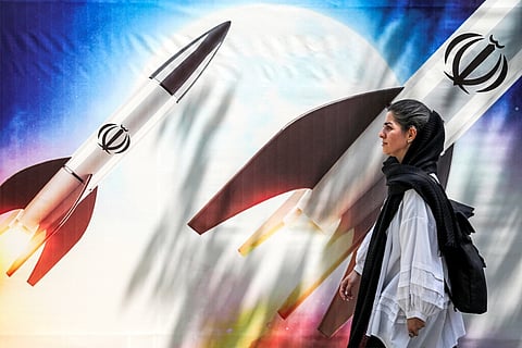 Uma mulher em Teerão passa junto de um cartaz que mostra mísseis iranianos a serem lançados.