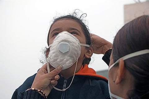 बढ़ते प्रदूषण में अपनी बच्ची की मास्क पहनने में मदद करती एक मां; फोटो: आईस्टॉक