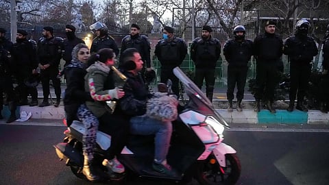 Policemen protect the British Embassy during a protest by hardline supporters of the Iranian government, as people ride on their motorbike in Tehran, Iran