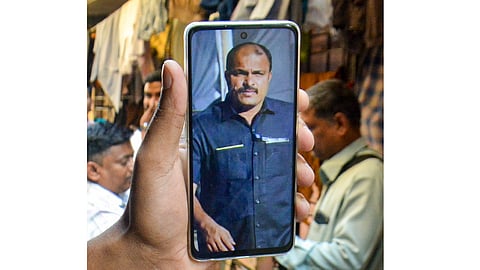 A man shows a photograph of Vidip Jadhav, one of the security personnel who died in the Baramati plane crash that also killed Maharashtra Deputy Chief Minister Ajit Pawar, as people gather outside Jadhav's house in Thane, Wednesday, Jan. 28, 2026 
